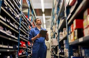 A man with a clipboard stands between warehouse shelves