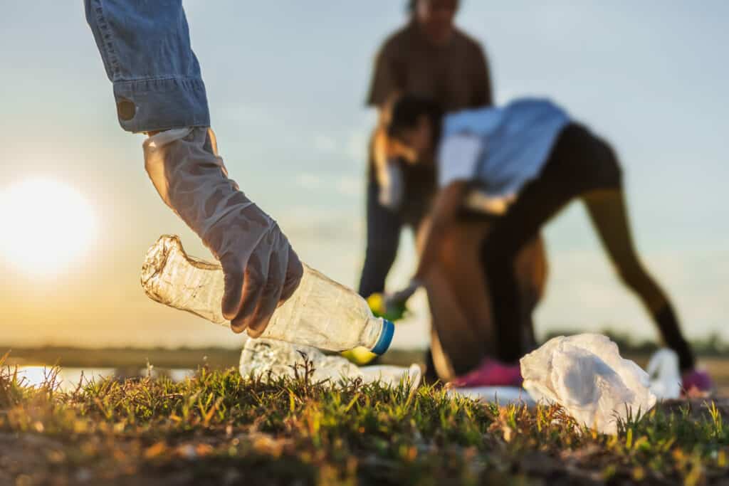 Three people pick up plastic bottles in a field