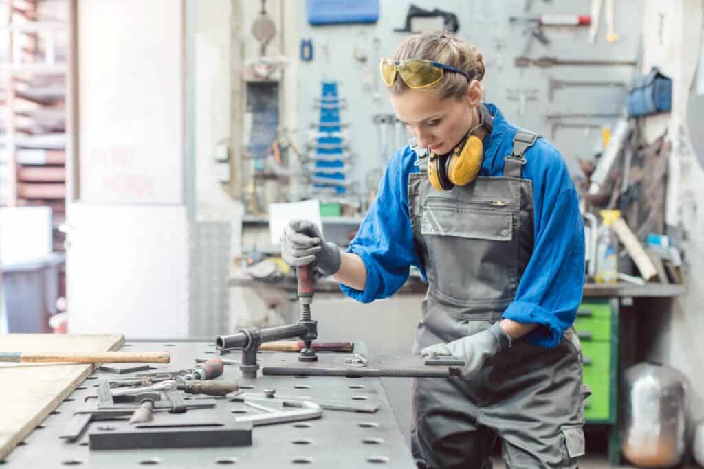 A woman in overalls and gloves using table-top machinery