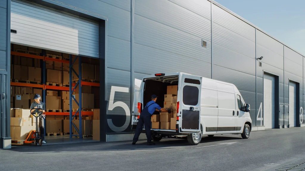 Workers loading a retail supplier delivery van at a warehouse loading bay